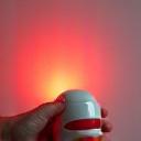 A modern, handheld red light therapy device emitting a soft, warm red glow.
